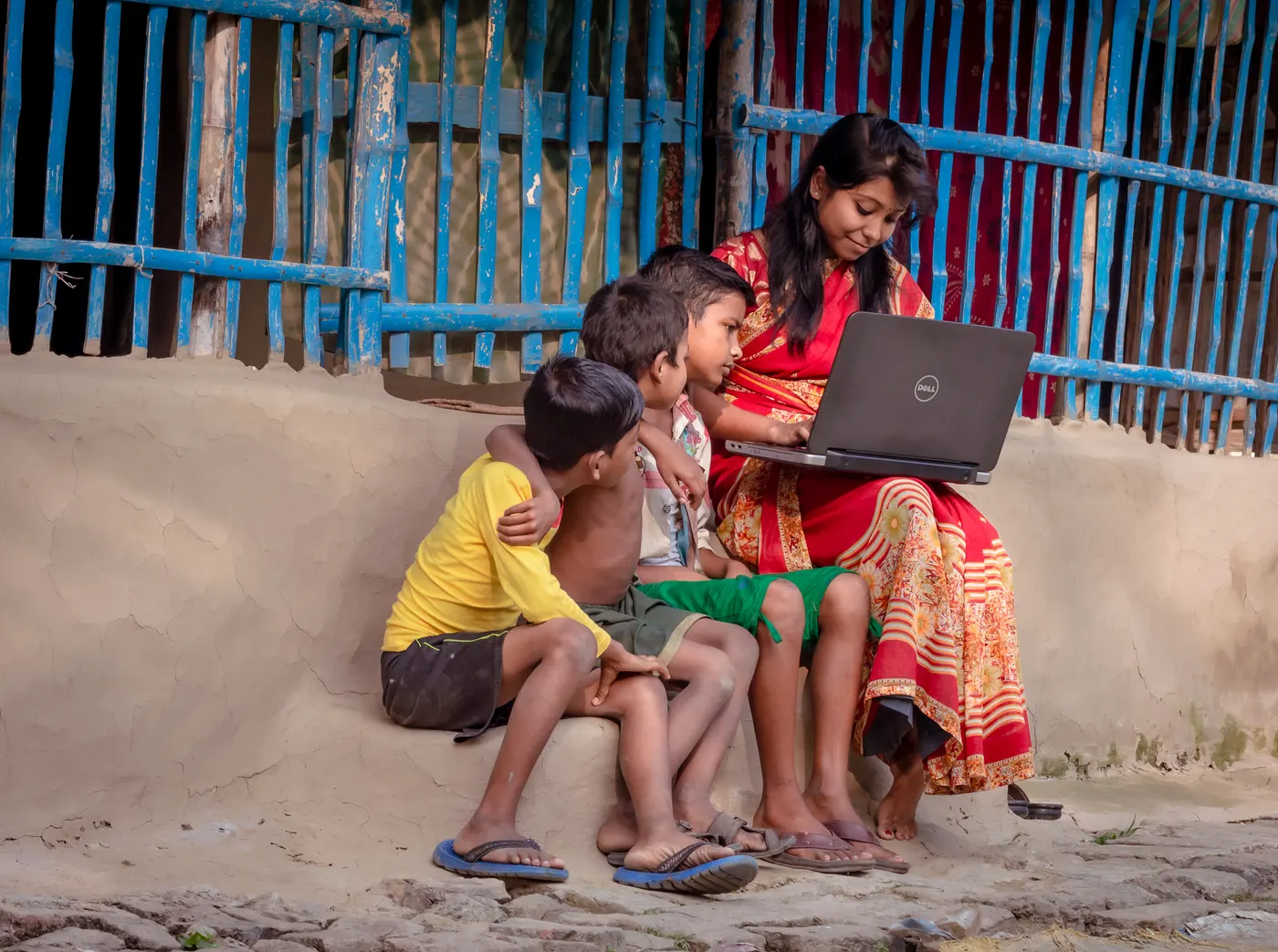A young woman sitting with a laptop while three children lean in to look at the screen