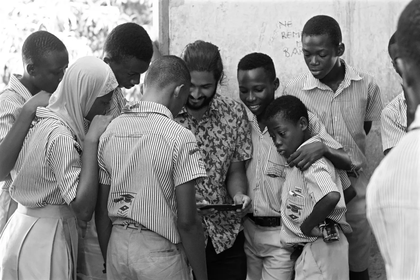 A teacher holding a phone while a group of students crowd around to look at the screen
